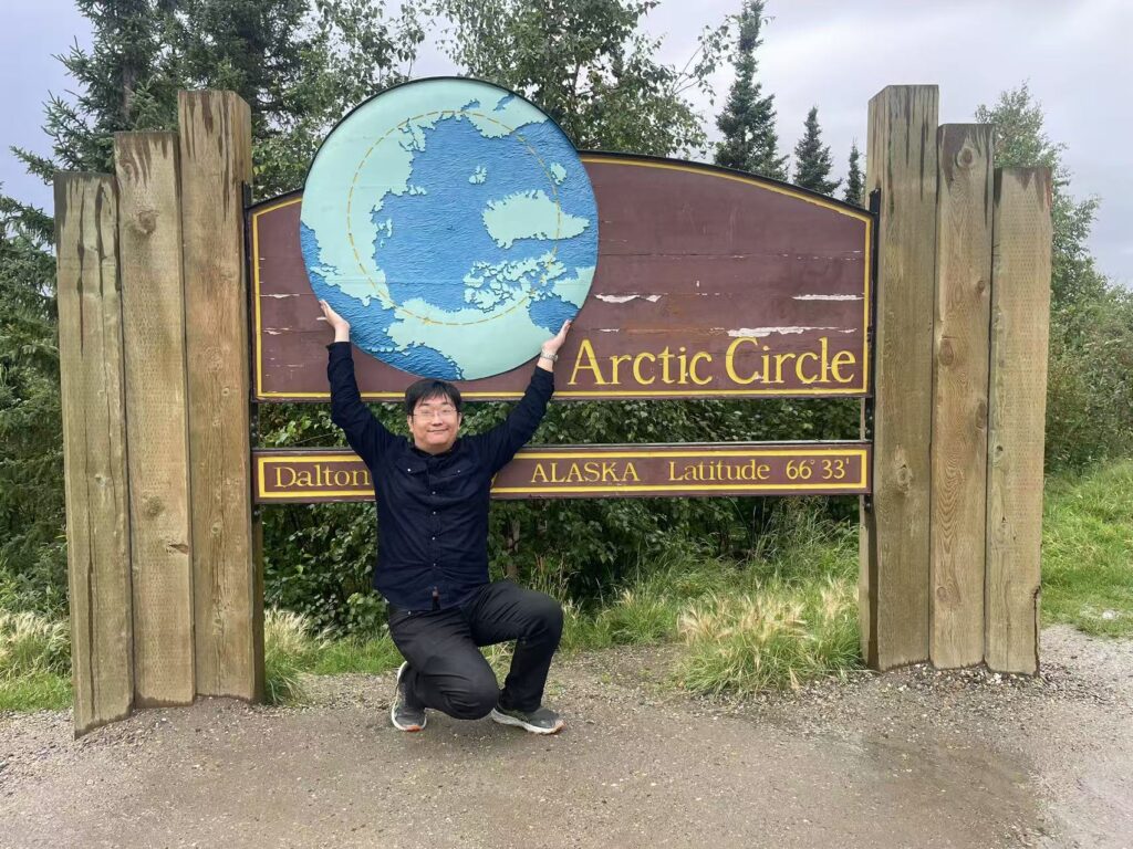 Muhao Chen at a sign marking the Arctic Circle, positioned as though he's holding up the earth.